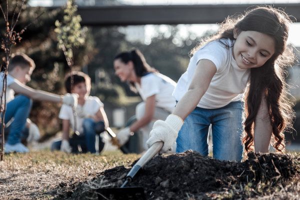 Young enthusiast. Nice pretty delighted girl holding a rake and using it while planting the tree